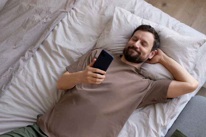 Man in bed smiling at phone